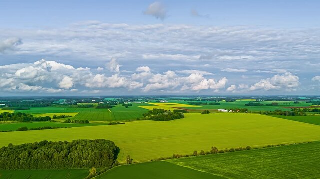 Aerial view of lush green agricultural fields and patches of forest under a cloudy sky in Latvia.