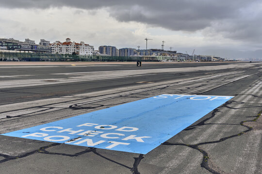 Gibraltar, Gibraltar - 01 March 2026: View of Joshua Hassan Gibraltar International Airport runway with blue FOD check point marking on asphalt, near buildings under cloudy sky.