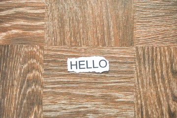 The word "HELLO" printed on a piece of torn white paper, placed on a brown parquet wooden surface. © Alvi Prasetya