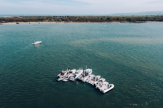 Poole, England, United Kingdom - 10 July 2021: Aerial view of motorboats rafted together in Poole Harbour, with people relaxing on deck under a clear blue sky.