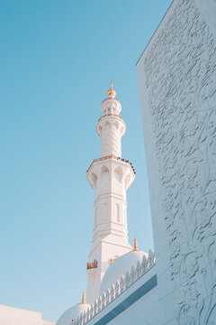 Abu Dhabi, United Arab Emirates - 20 April 2024: View of the minaret and ornate white marble walls of the Sheikh Zayed Grand Mosque under a clear blue sky.