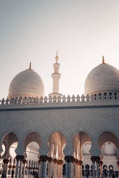 Abu Dhabi, United Arab Emirates - 20 April 2024: View of the Sheikh Zayed Grand Mosque featuring white marble domes, a tall minaret, and intricate arched colonnades under a clear sky.