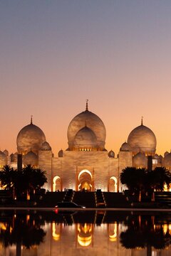 Abu Dhabi, Abu Dhabi, United Arab Emirates - 20 April 2024: View of the Sheikh Zayed Grand Mosque at sunset, with its white domes, arches, and reflection in the foreground pool.