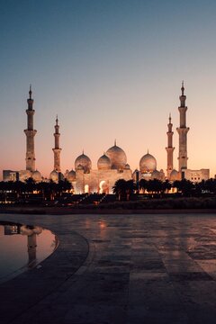 Abu Dhabi, United Arab Emirates - 20 April 2024: View of the Sheikh Zayed Grand Mosque at dusk, featuring its white marble domes, minarets, and reflecting pools under a soft sunset sky.