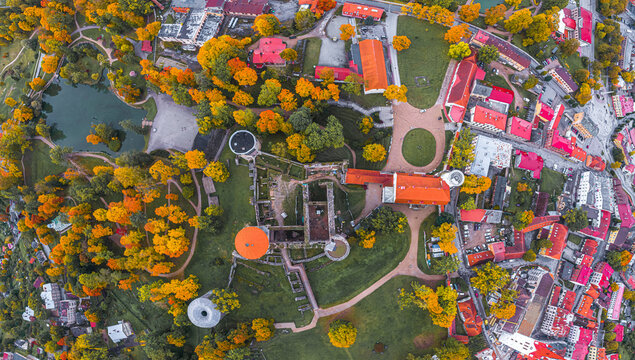 Aerial view of Cesis Castle surrounded by vibrant autumn foliage, historic stone ruins, and park paths in the town of Cesis, Cesis Municipality, Latvia.