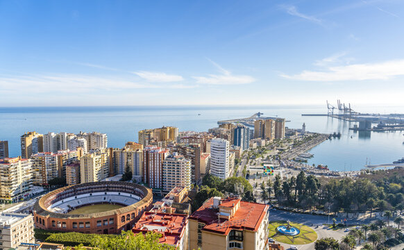 View of the panoramic cityscape of Malaga featuring the Plaza de Toros de La Malagueta, the bustling port, and the Mediterranean Sea under a clear blue sky in Malaga, Andalusia, Spain.