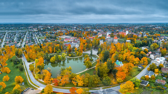 Aerial view of Cesis Castle ruins surrounded by vibrant autumn foliage, a serene pond, and the historic townscape of Cesis, Cesis Municipality, Latvia.
