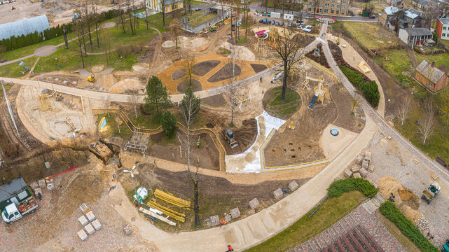 Aerial view of a park construction site with new playground equipment, dirt paths, and landscaping work in progress in Latvia.