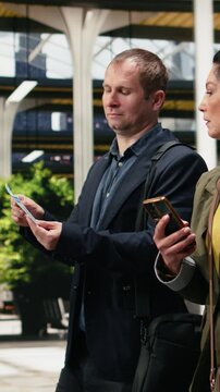 Vertical frame: Business travelers compare a printed bus ticket with information on a smartphone inside a terminal; the companions review boarding pass details and mobile navigation before departure.