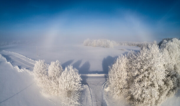 Aerial view of a snow-covered landscape with frost-covered trees and a sun halo in the clear blue sky in Latvia.