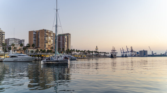 Malaga, Andalusia, Spain - 10 January 2020: View of the Malaga port, promenade and Palmeral de Las Sorpresas with docked yachts and sailboats under a clear sky.