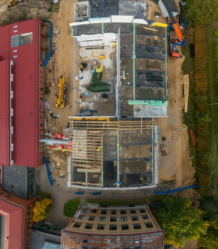Aerial view of a construction site featuring building foundations, cranes, and surrounding structures in Latvia.
