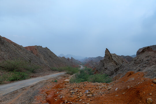 View of the Sulaiman Mountains with a winding road through rugged rocky terrain, red soil, and sparse vegetation in De-excluded Area Dera Ghazi Khan, Punjab, Pakistan.