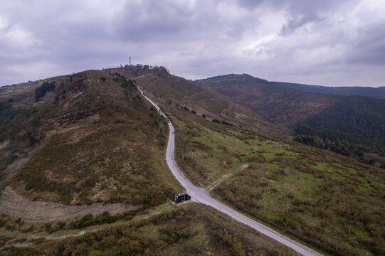 Aerial view of a camper van parked on a winding dirt road traversing the rolling green hills of the Basque countryside in Gaztelugatxeko Doniene, Euskadi, Spain.