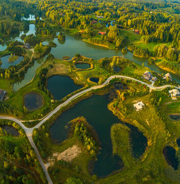Aerial view of a lush green landscape featuring interconnected lakes, winding roads, and scattered houses in Latvia.