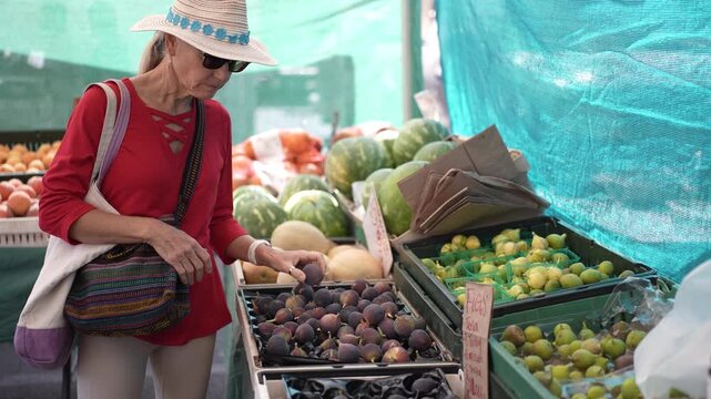 A mature woman smiles as she picks fresh figs at the Farmers Market in Sonoma, California on a sunny morning