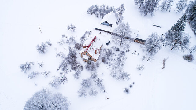 Aerial view of a house surrounded by snow-covered trees and fields in a winter landscape, Latvia.
