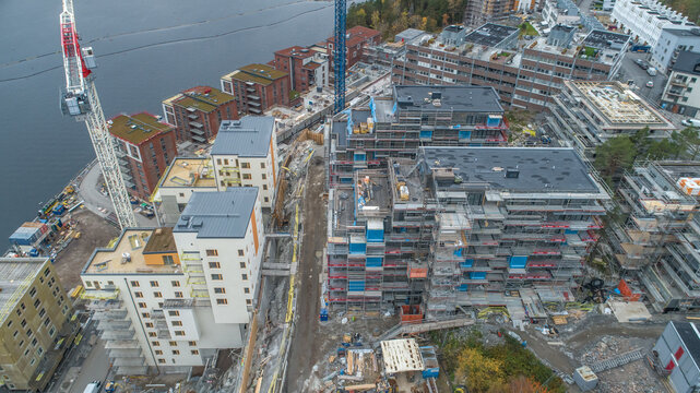 Aerial view of a modern residential construction site featuring cranes, scaffolding, and partially completed apartment buildings situated along a waterfront in Sweden.
