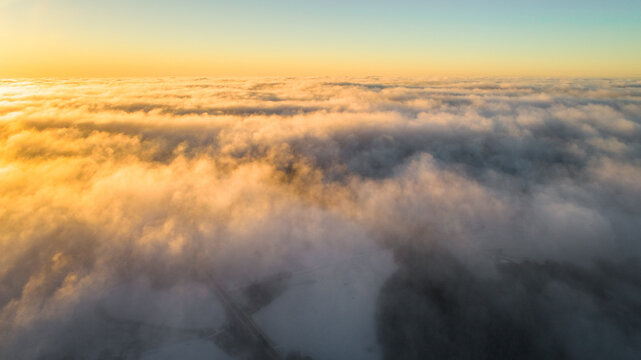 Aerial view of a thick layer of clouds illuminated by the golden light of sunset over the landscape of Latvia.
