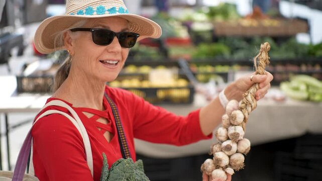 Mature woman smiles as she buys a braid of garlic at the Sonoma Farmers Market on a sunny morning in California.