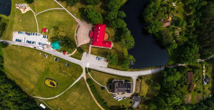 Dunte, Latvia - 01 June 2019: Aerial view of Munchhausen Museum surrounded by lush green parkland, a small lake, and parking areas in the Latvian countryside.
