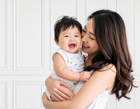 白い装飾壁の前で笑顔の赤ちゃんを抱き寄せる母親
