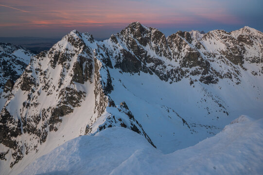 View of Koprovsky stit with snow-covered mountain peaks under a twilight sky in Vysoke Tatry, Presov Region, Slovakia.