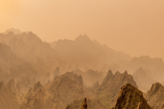 View of the rugged peaks of the Sulaiman Mountains under a hazy, golden sky in the De-excluded Area Dera Ghazi Khan, Punjab, Pakistan.