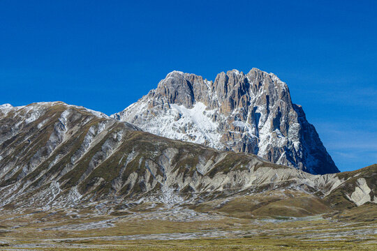 View of Gran Sasso d'Italia with snow-capped peaks and rocky slopes under a clear blue sky in Pietracamela, Abruzzo, Italy.