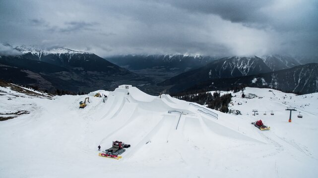 Aerial view of the snow park at Watles ski resort with snow grooming machines preparing the slopes under a cloudy sky in Mals, Trentino-Alto AdigeS, Italy.
