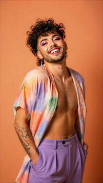 Confident Young Queer Man with Makeup and Tie-Dye Shirt Smiling on Orange Background