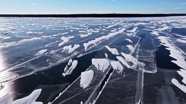 Aerial view of frozen lake with intricate snow patterns and ice cracks covering the surface in Latvia.
