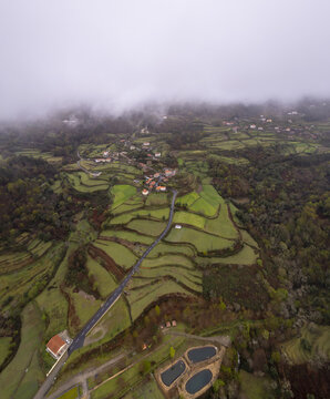 Aerial view of terraced green fields, a winding road, and small houses nestled in the misty hills of Sobrada, Viana do Castelo, Portugal.