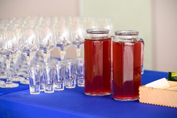 Glass jug with traditional red berry drink berry juice or mors served next to empty wine glass and shot glass during a catered event buffet. © Tatiana