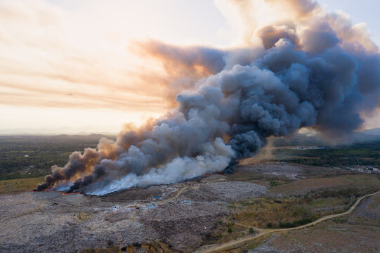 Aerial view of the Vertedero duquesa landfill engulfed in flames with a massive plume of smoke rising into the sky at sunset, Pantoja, Santo Domingo, Dominican Republic.