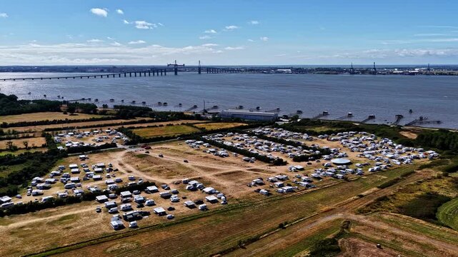 Aerial view of a large campsite filled with caravans and campers situated along the riverbank with a bridge in the background in Bordeaux, Nouvelle-Aquitaine, France.