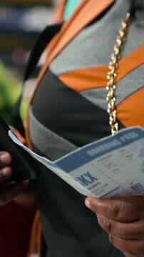 Vertical frame: Close-up: A traveler checking a bus ticket and verifying the route on a mobile phone, confirming printed journey details with a smartphone inside the shuttle terminal before departure.