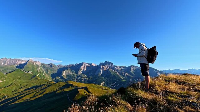 Aerial view of a hiker sitting on a grassy ridge overlooking the vast Col d'Aubisque mountain range under a clear blue sky in Beost, Nouvelle-Aquitaine, France.