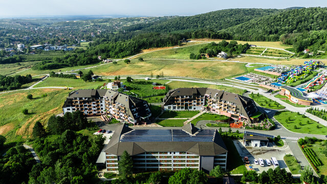 Aerial view of the Movenpick Resort and Spa Fruske Terme featuring modern hotel buildings, a large water park with colorful slides, and green hills in Vrdnik, Vojvodina, Serbia.
