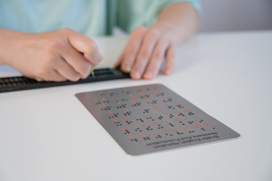 A blind woman writes in Braille using a stencil on a piece of paper. 