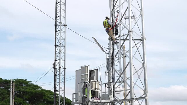 Telecommunication tower technician safety harness maintenance antenna network infrastructure climbing, high altitude worker repairing cellular equipment and cables on steel lattice mast under blue sky
