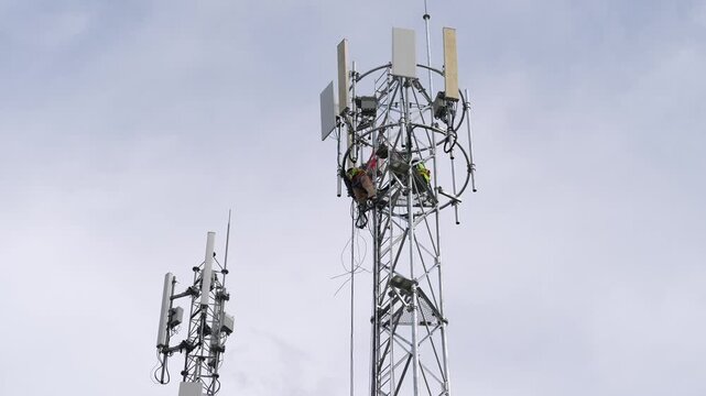 Cell tower antenna technician and worker maintenance for telecom network wireless communication and signal during equipment installation, climbing high mast with safety harness adjusting cables