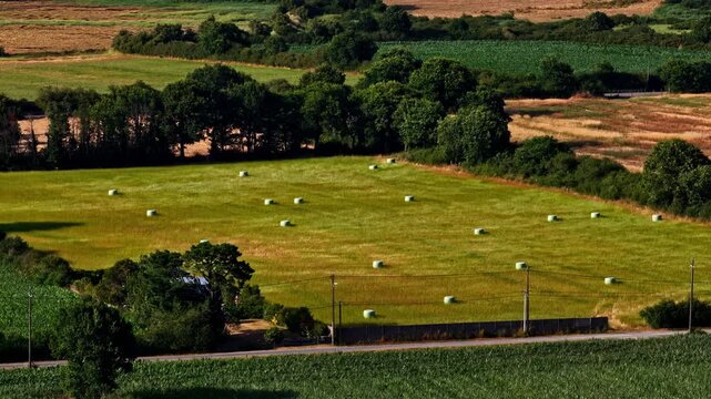 Aerial view of hay bales scattered across a green agricultural field bordered by trees and a road in Nantes, Pays de la Loire, France.
