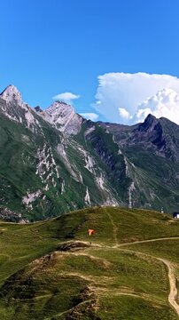 Aerial view of a paraglider soaring above the green slopes and dirt trails of Col d'Aubisque in Beost, Nouvelle-Aquitaine, France.