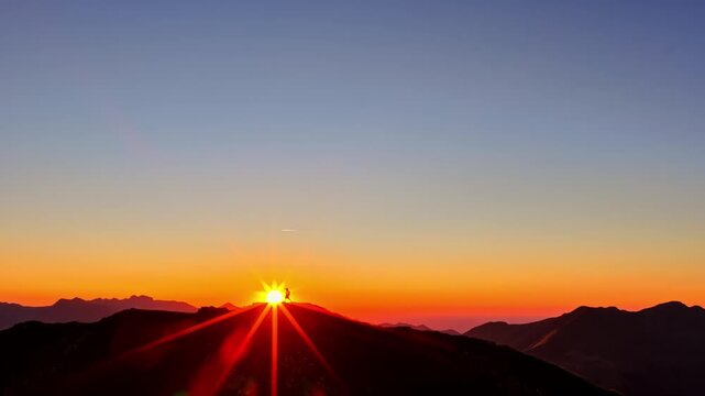 Aerial view of a person silhouetted against the vibrant orange sky on the mountain ridge of Col d'Aubisque in Beost, Nouvelle-Aquitaine, France.