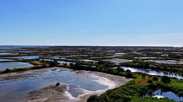 Aerial view of salt marshes and wetlands with lush green vegetation and water pools under a clear blue sky in Capbreton, Nouvelle-Aquitaine, France.