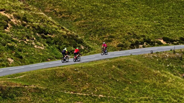 Aerial view of two cyclists riding along the winding mountain road of Col d'Aubisque surrounded by green grassy slopes in Beost, Nouvelle-Aquitaine, France.