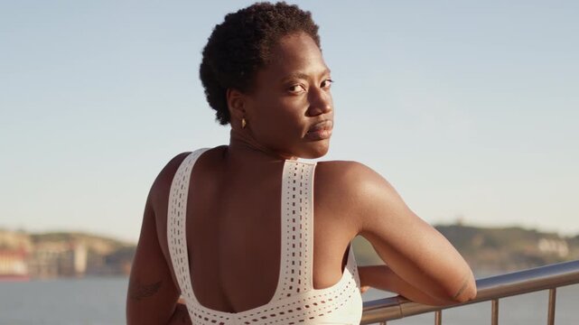 Back view of a Black African American woman standing by a railing and looking over the city after an outdoor fitness session.