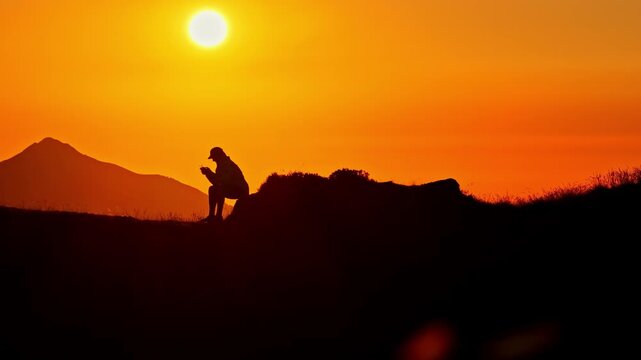 Aerial view of a silhouette of a person sitting on a ridge at Col d'Aubisque during a vibrant sunset in Beost, Nouvelle-Aquitaine, France.