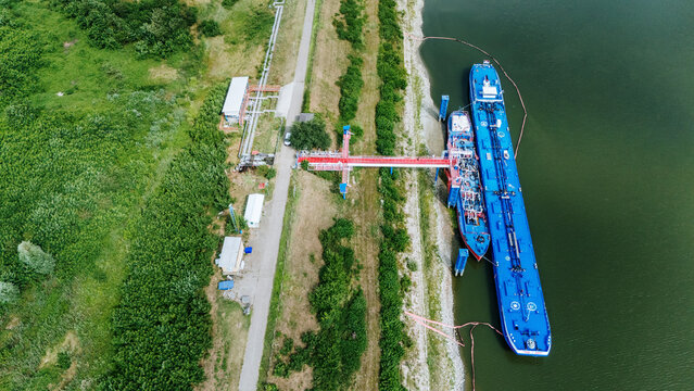 Aerial view of Luka Novi Sad with blue cargo ships docked at the riverbank, red loading infrastructure, and surrounding green vegetation in Novi Sad, Vojvodina, Serbia.